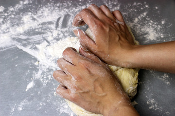A woman kneads sweet yeast dough on the grey table