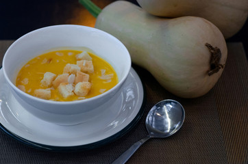 Butternut squash soup with pieces of bread biscuit on dark wooden background, near fresh butternut