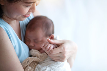 Asian mother is holding and looking at newborn baby in her arms. her hands hold the baby's hands, happy mother and baby enjoy spending time together