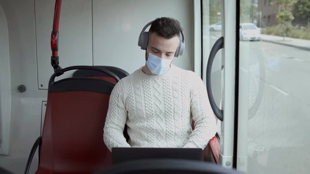A man in a mask works with the computer while traveling on a public transport urban bus