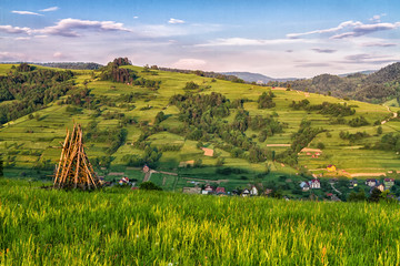 Traditional Slovenian constructions for drying hay and wood storage, hayrack on the hilly field in Beskid Sadecki mountains, Poland. Lomnica Zdroj and Piwniczna towns in the background.