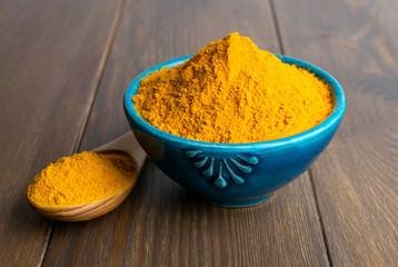 Turmeric powder in blue bowl with wooden spoon at wooden background.