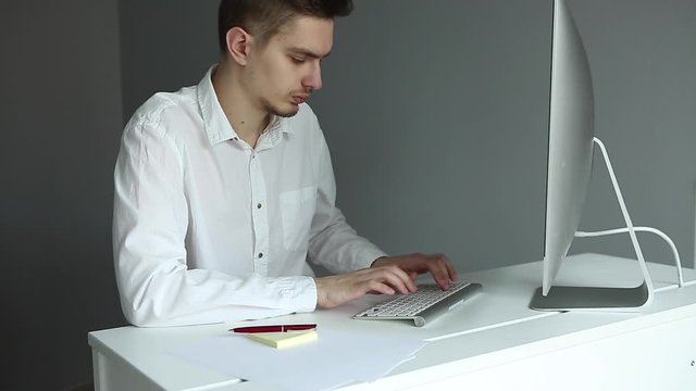 Young man in white shirt working at the desktop with a computer in office. Worker on grey background