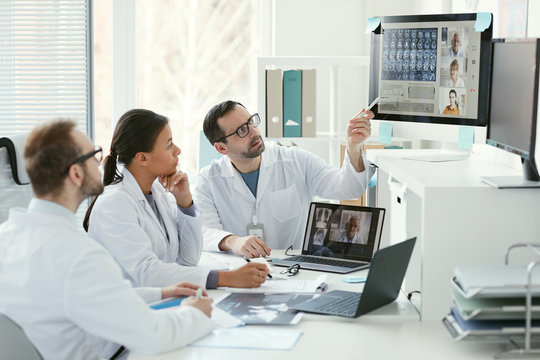 Doctor pointing at computer monitor and discussing x-ray images with his colleagues during online conference