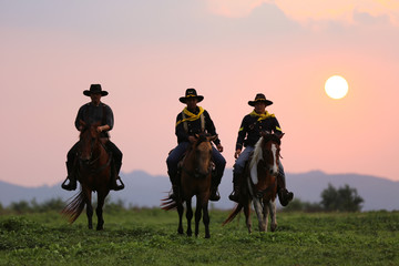 Silhouette of western riders against amber colored sunset
