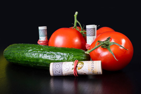 Red tomatoes and cucamber shown with money. Profits, price and costs related to vegetables.