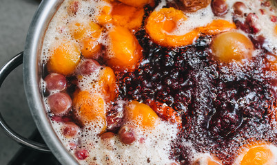 Fresh fruits: apricots, cherries, raspberries, apples are boiled in boiling water in a metal pan on a stove with bubbles and foam close-up. Cooking delicious homemade compote. Photography, concept.