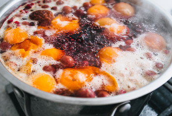 Fresh fruits are boiled in boiling water in a metal pan on a stove with bubbles and foam close-up. Cooking a delicious compote of apricot, apples, cherries, raspberries. Photography, concept.