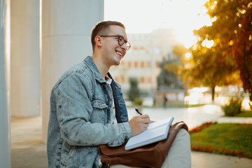 Young student studying for term exam in the park outdoors. Stylish man working at univervisty campus.