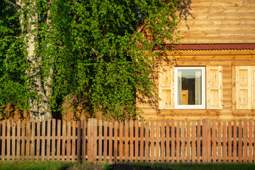 The wooden house is lit by the setting sun. Colorful view of a country house and birch.