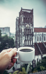 coffee Cup in hand against the background of a Catholic Church in Hanoi