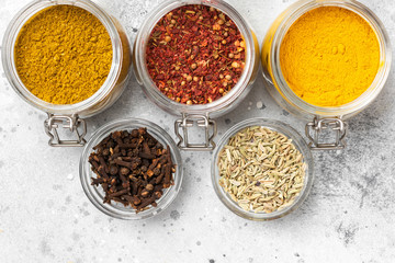 Spices and condiments in glass jars on a light gray table. Spices close-up with space for text. The view from the top