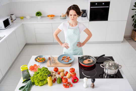 Photo of beautiful housewife lady look unsure boiled shrimps cooking gourmet family dinner prepared ingredients forgot something arms by sides wear apron t-shirt modern kitchen indoors