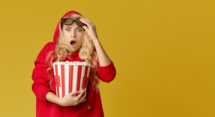 Shocked young models woman in 3d glasses eating popcorn, looks scary Movie at the cinema. Isolated on yellow background