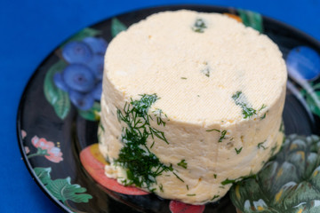 a piece of homemade cheese with dill and spices on a black plate