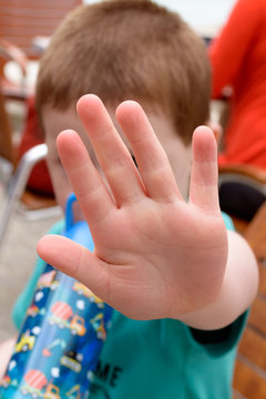 Concept of saying stop or no: small child holding up the palm of his hand. He could be a victim of domestic violence / abuse or simply refusing to have his photograph taken