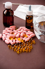 Medical still life: tablets, fish oil, medical mask, a mug of water and medicine in bottles on a brown background