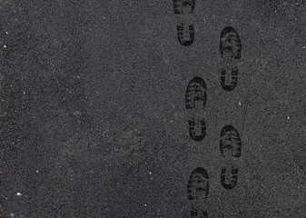 Black wet footprints over gray pedestrian asphalt road