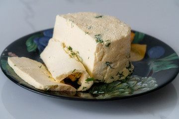 a piece of homemade cheese with dill and spices on a black plate