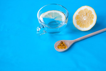 Wooden spoon with fish oil, cut lemon and a Cup with water and a slice of lemon on a blue background, place for text