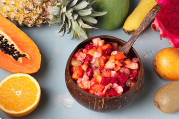 Tropical fruit salad in coconut bowl on a light blue background, Horizontal format