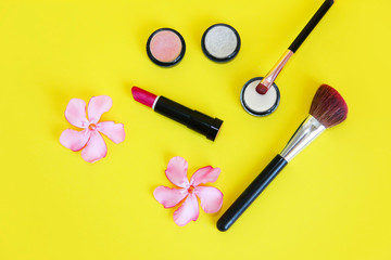 Obraz na płótnie Canvas decorative cosmetics, powder, eye shadow, lipstick, lip gloss, makeup brushes and pink flowers