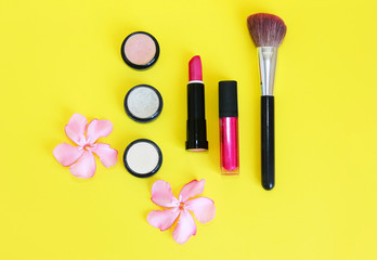Obraz na płótnie Canvas decorative cosmetics, powder, eye shadow, lipstick, lip gloss, makeup brushes and pink flowers
