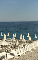 white umbrellas and empty sunbeds on the beach, sea view