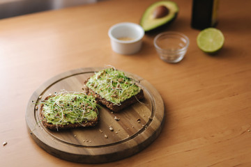 Vegan toast with guacamole on wooden board. Rye toasted bread with avocado on top. Background of ingredients. Avocado, lime, olive oil