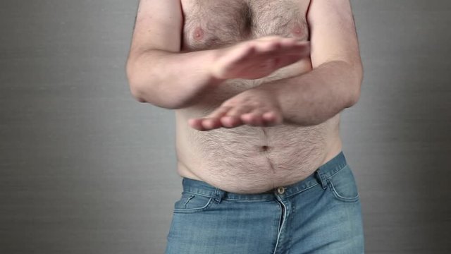 Happy shirtless fat man in jeans dancing in slow motion with hands scissors. Big obese belly shaking. Overeating problem concept