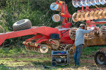 The farmer repairs the harrows if they are damaged by hitting stones. A master welder welds metal parts of agricultural equipment. © Niko_Dali