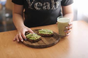Close up of woman hold toast with guacamone in one hand and smoothie in another. Vegan lunch