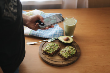 Fototapeta na wymiar Woman make photo of lunch at home. Female glogger make food photography. Healthy vegan food. Toast with avocado and smoothie with spinach