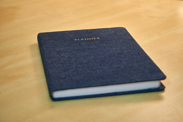 Planner or organizer notebook with jeans texture material cover, a diary to make appointment meeting or manage timetable close book on a wooden office desk 
