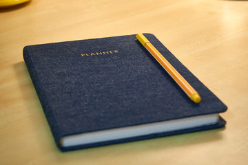 Planner or organizer notebook with jeans texture material cover and a yellow pen, a diary to make appointment meeting or manage timetable close book on a wooden office desk 