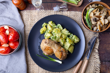 Chicken with potatoes, salted tomatoes and pickled mushrooms. In the background is a glass of vodka, a decanter, a salt shaker, onion and garlic. Rustic style.