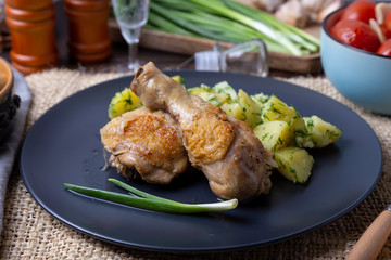 Chicken with potatoes, salted tomatoes and pickled mushrooms. In the background is a glass of vodka, a decanter, a salt shaker, onion and garlic. Rustic style.
