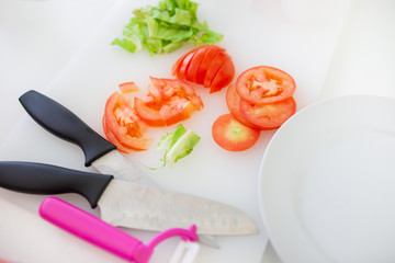 slice tomoto and organic vegetables on plastic butcher, metal knife in kitchen room