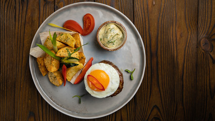 Beef medallions with egg, potatoes and peppers on a wooden background