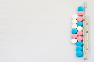 multicolored pills of vitamins and an old thermometer