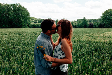 naturally defocused caucasian couple in casual clothes kissing in a greenfield - focus on the field