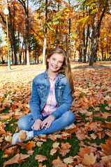Autumn portrait of adorable smiling little girl child preteen sitting in leaves in the park