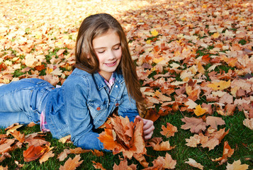 Autumn portrait of adorable smiling little girl child preteen lying in leaves in the park