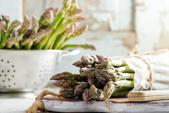 Bunch of raw organic asparagus on a board and in a colander ready for cooking healthy diet food on a light grey marble background. - Powered by Adobe