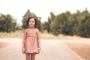 Smiling cute child girl 4-5 year old wearing stylish dress posing in park outdoors closeup. Summer time. Vacation season.