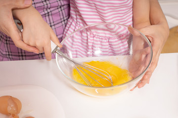 Little cute girl and her mother beat eggs for dough in the kitchen at home, concept of a happy family