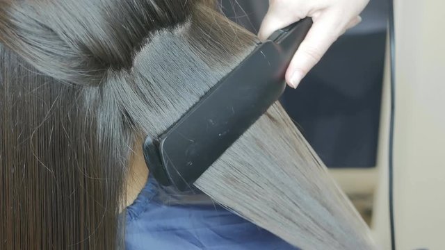 A hairdresser makes hair alignment for a woman using a special hair straightener. Keratin hair straightening. The alignment of the curls of hair. 4K