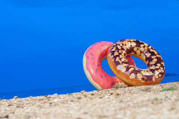 Closeup Rubber Float Ring shape of pink Donut and chocolate beans doughnut on the beach at night in summer and blue sky in holiday.
