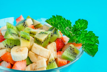 fruit salad in a glass plate on a blue background. salad of kiwi, bananas, apples, berries, mint. A large number of vitamins. fitness salad.
