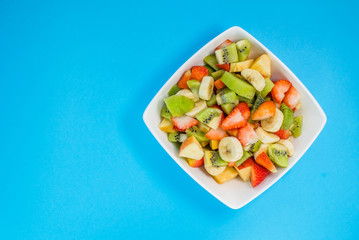 fruit salad in a white plate on a blue background. salad of kiwi, bananas, apples, berries, mint. A large number of vitamins. fitness salad.